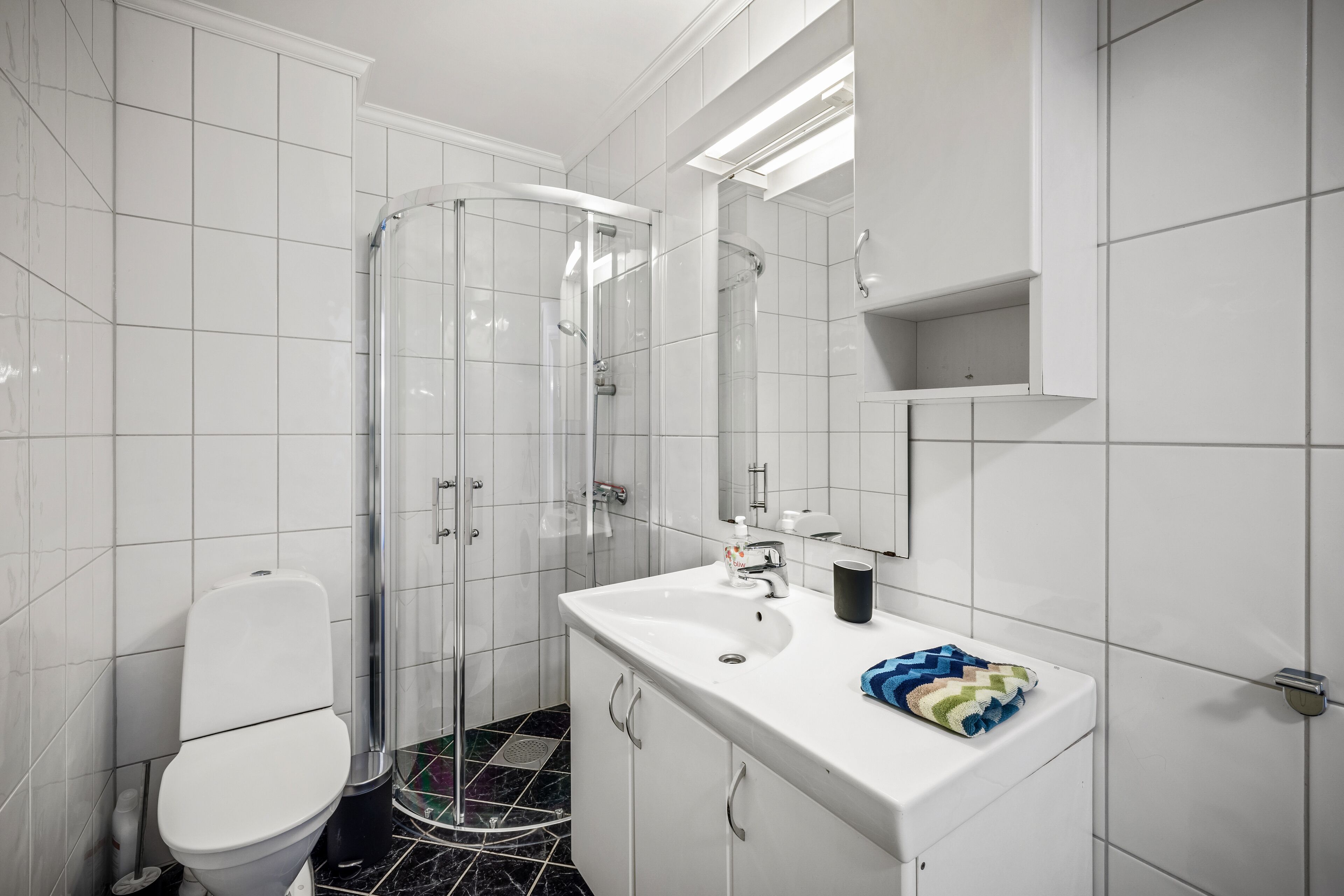 A modern bathroom with a white toilet, a glass shower enclosure, a white sink with a mirror, and a tiled floor.