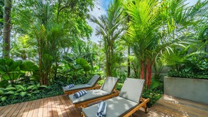 A wooden deck with three sun loungers, surrounded by lush tropical plants. - Villa Satiya (Munggu)