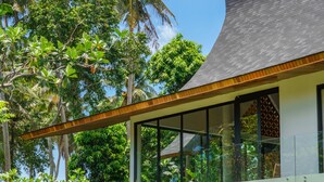 A modern house with a large glass balcony, surrounded by lush greenery and palm trees. - Villa Satiya (Munggu)