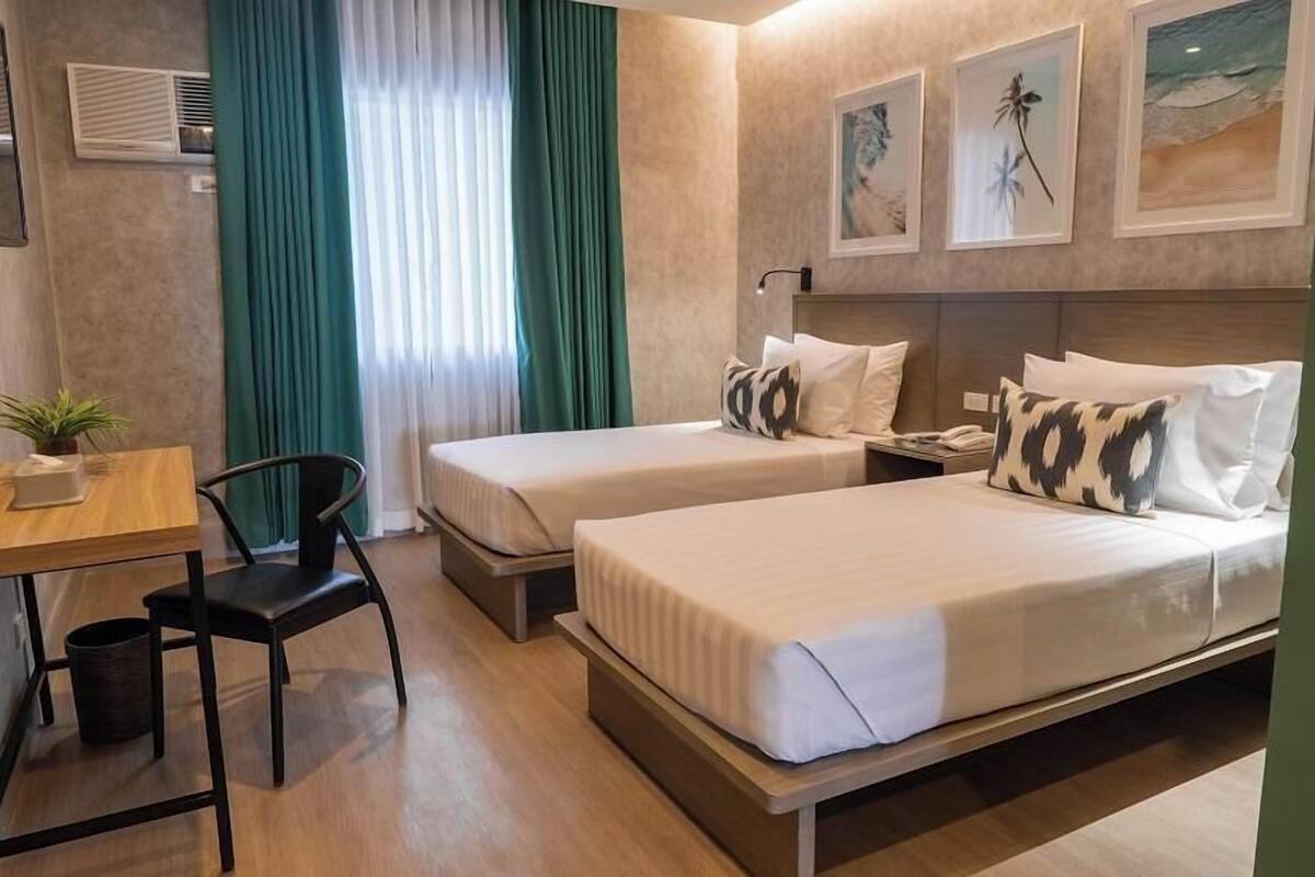 A hotel room with two beds, a desk, a chair, and a window with curtains.