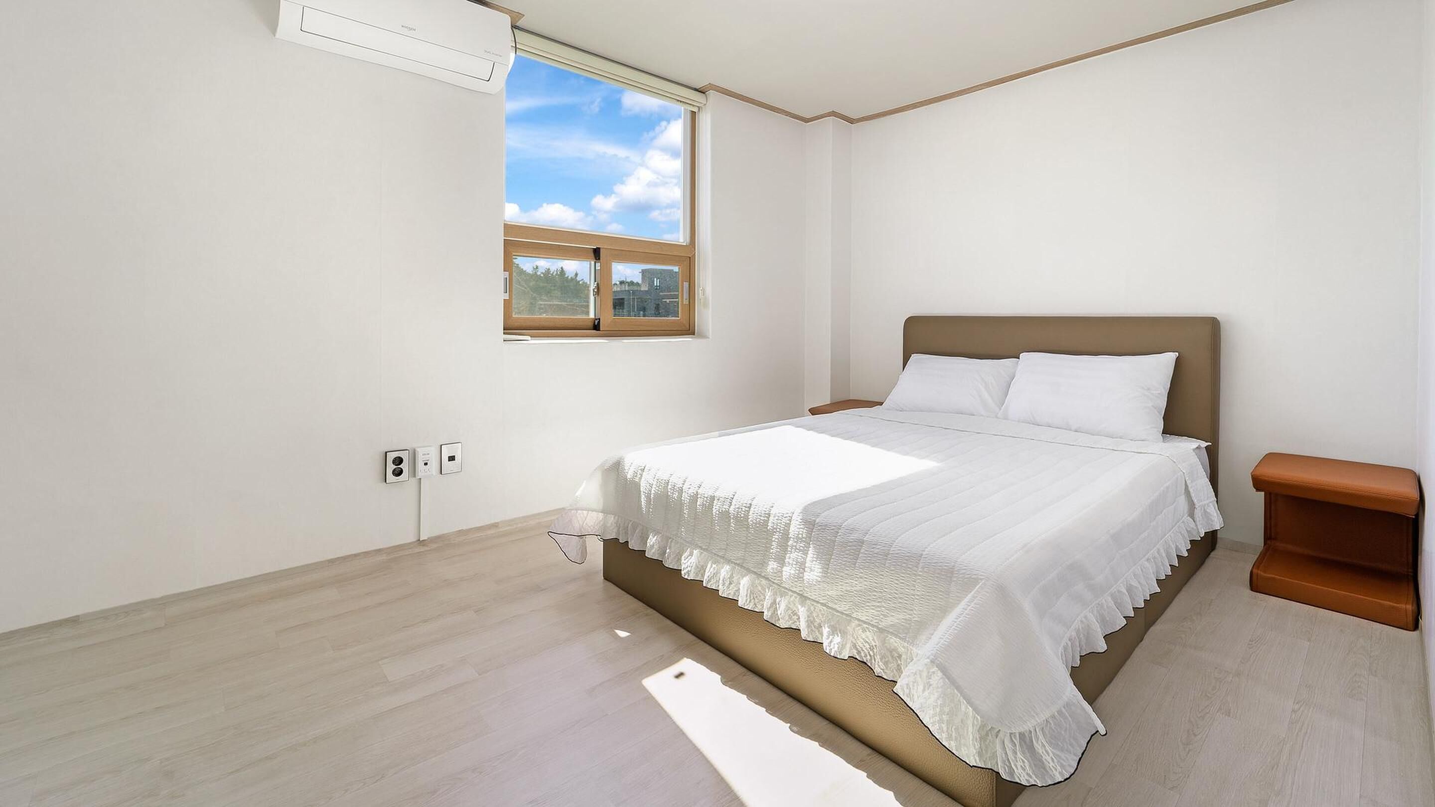 Une chambre à coucher comprenant un lit, une table de chevet, une fenêtre et un appareil de climatisation.
