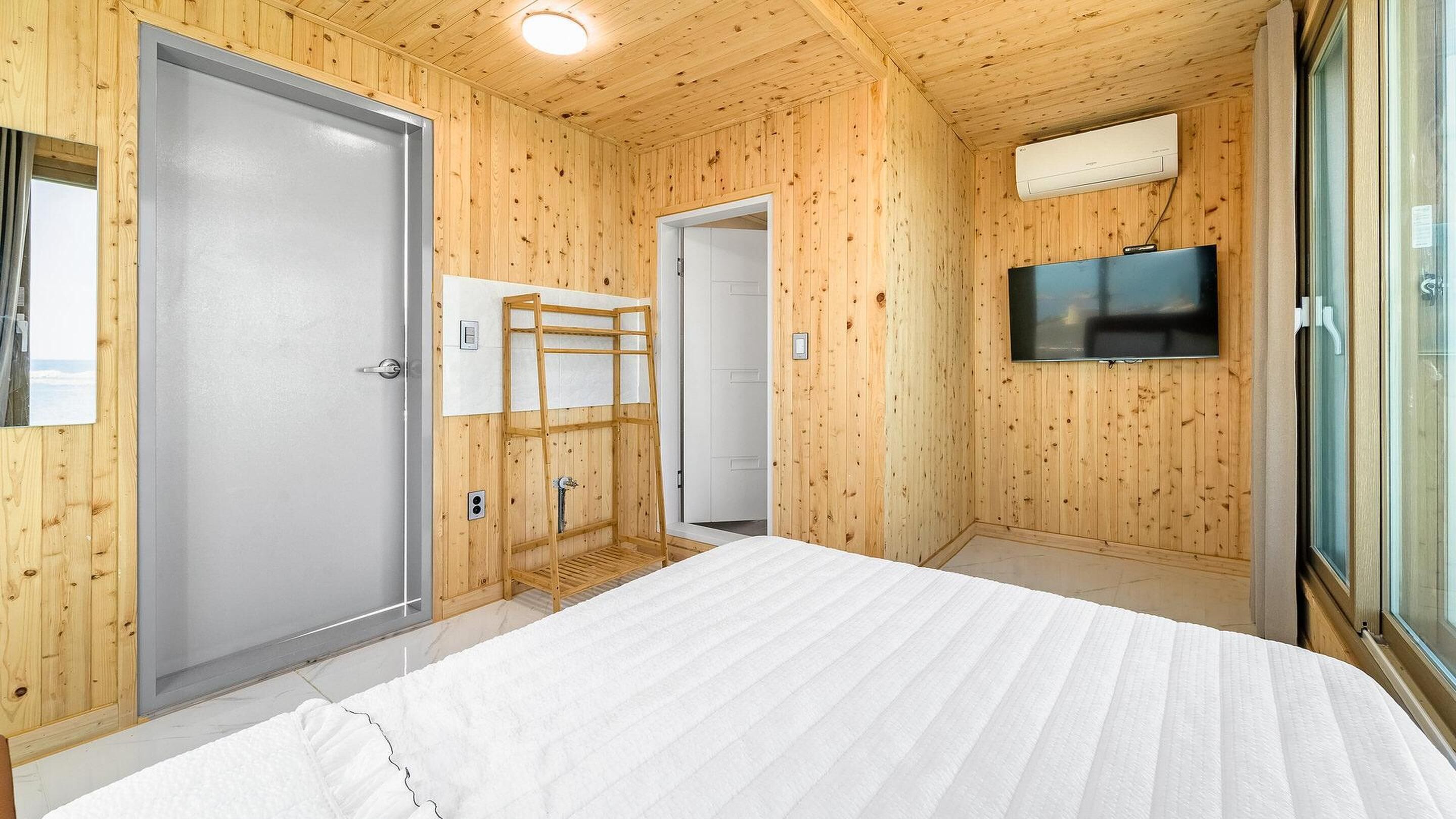 Une pièce aux murs lambrissés, comprenant un lit, un téléviseur et un espace douche.