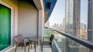 Un balcón con dos sillas de mimbre y una mesita redonda, con vistas a un paisaje urbano de edificios altos.