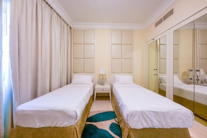 Une chambre d’hôtel avec deux lits simples, une table de chevet avec une lampe, un miroir et un grand meuble-miroir.