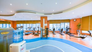 Un gimnasio con varios equipos de ejercicio, un dispensador de agua y ventanas amplias.