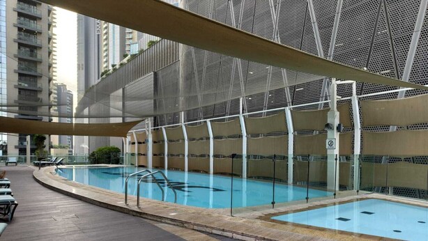 Una piscina interior con diseño moderno, rodeada por una zona cubierta con asientos y vistas a edificios altos.
