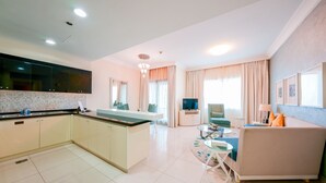 Una cocina moderna con una isla central, un comedor con sofá y mesa de centro, y una sala de estar con televisor y asientos.