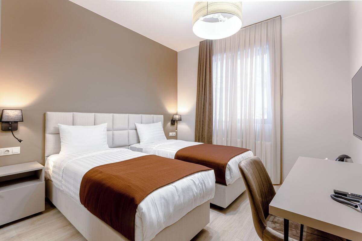 A hotel room with two beds, a desk, and a television.