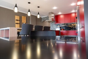 A modern kitchen with red cabinetry, a stainless steel range hood, and pendant lighting.