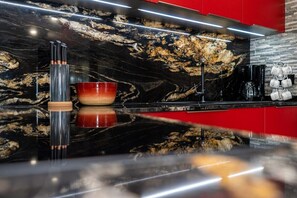 A modern kitchen with a black marble backsplash, stainless steel appliances, and a red accent wall.