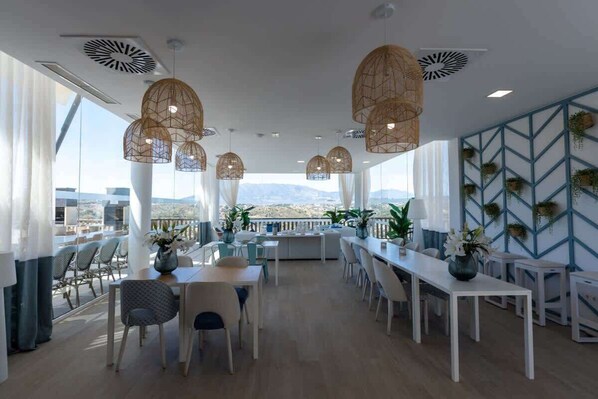 A spacious dining area with white furniture, hanging wicker lamps, and a view of the mountains.