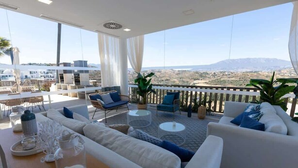 Een balkon met een witte bank, blauwe stoelen en een tafel met decoratieve objecten.