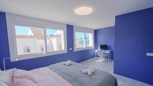 Ein Schlafzimmer mit einem Bett, zwei Fenstern, einem Schreibtisch und einem Stuhl.