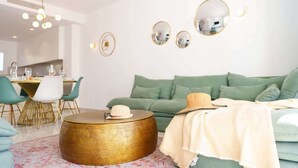 Ein modernes Wohnzimmer mit einem grünen Sofa, einem runden Couchtisch und einem Essbereich mit weißem Tisch und Stühlen.