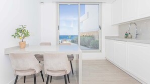 A modern kitchen with a view of the sea, a dining area with chairs, and a potted plant.
