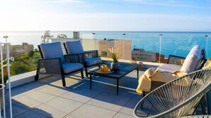 A terrace with seating, a table, and a view of the sea.