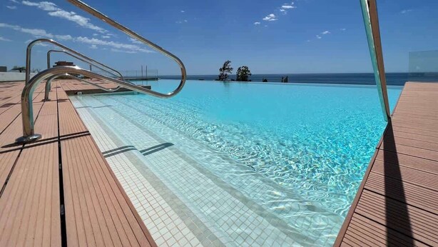 A pool with clear water, a wooden deck, and a metal railing.