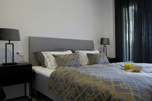 A hotel room with a bed, two bedside tables with lamps, a window with curtains, and a breakfast tray with a glass of orange juice and a bowl.