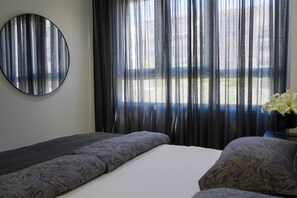 A hotel room with a bed, a round mirror, and a window with sheer curtains. - Cala Serena  ·  Beautiful 3 bedroom apartment 850 meters from the beach in La Cala de Mijas (La Cala de Mijas)