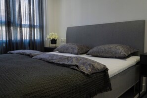 A bed with a grey headboard, a dark grey blanket, and patterned pillows.