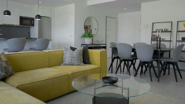A modern living room with a sofa, a glass coffee table, and a dining area with chairs and a table. - Cala Serena  ·  Beautiful 3 bedroom apartment 850 meters from the beach in La Cala de Mijas (La Cala de Mijas)