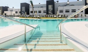 A swimming pool with a tiled deck, metal railings, and lounge chairs.