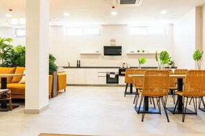 Una cucina moderna con mobili bianchi, un forno a microonde nero e un'area pranzo con sedie in vimini.