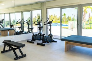 Une salle de sport équipée de matériel d’exercice, d’un banc et de grandes fenêtres donnant sur une piscine.