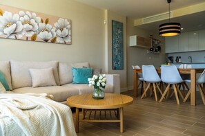 Una sala de estar moderna con un sofá, una mesa de centro redonda con un florero y un comedor con sillas y una mesa.