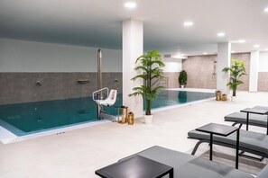 Una piscina interna moderna con acque cristalline, circondata da zone relax e piante in vaso.