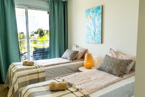 A hotel room with two beds, a balcony, a painting, and a lamp.