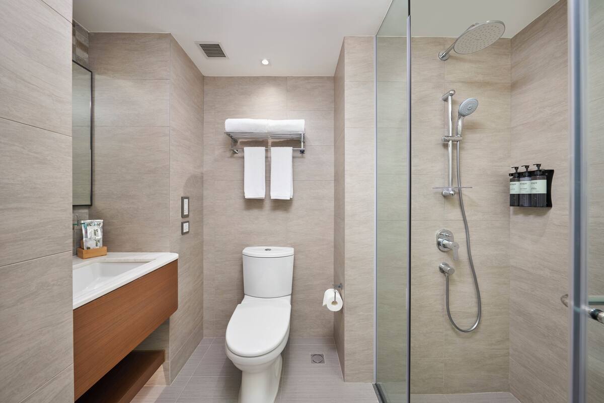 A modern bathroom with a toilet, a glass-enclosed shower, and a wooden vanity.