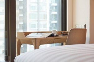 Habitación de hotel con un ventanal grande, un escritorio de madera con una computadora portátil, una taza y un par de lentes.
