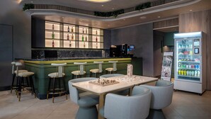 Zona de bar moderna con mostrador de mármol, taburetes, una mesa de ajedrez y una máquina expendedora de bebidas.