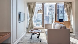 Una habitación de hotel moderna con un ventanal grande, un sofá, una mesa y un televisor montado en la pared.