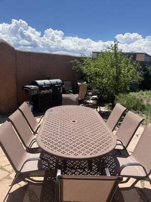 Eine Terrasse im Freien mit einem runden Tisch, sechs Stühlen, einem Grill und einem Baum.
