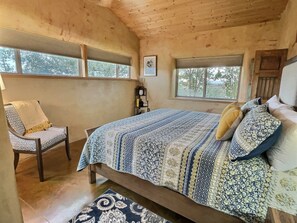 Ein gemütliches Schlafzimmer mit einem großen Bett, zwei Fenstern, einem Sessel und einem kleinen Tisch.