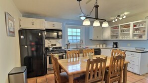 A kitchen with white cabinets, a black refrigerator, a stove, and a dining table with wooden chairs. - Sweet Adobe Convenient to Taos and Taos Ski Valley (Taos)