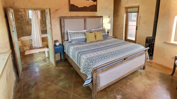 A bedroom with a large bed, wooden walls, a small bedside table, and a window. - Sweet Adobe Convenient to Taos and Taos Ski Valley (Taos)