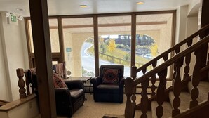 A cozy lobby with a staircase, a view of a winding road, and two leather sofas with throw pillows. - So Close to the Slopes (Taos Ski Valley)