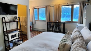 A bedroom with a bed, a desk, and a chair. There is a window with curtains, a microwave, and a shelf with a fan. - So Close to the Slopes (Taos Ski Valley)