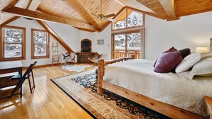 A cozy loft bedroom with a large bed, wooden beams, and a fireplace.