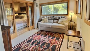 A cozy room with a bed, a sofa, a patterned rug, and a window with a view of trees.