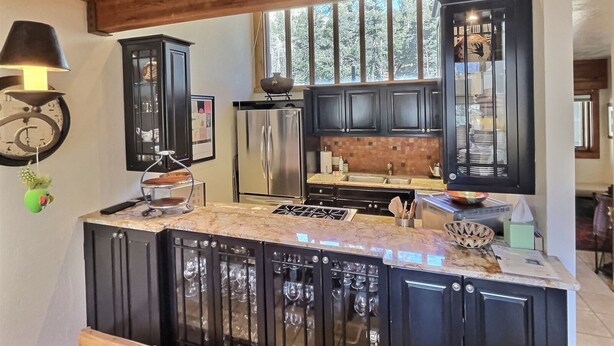 A kitchen with dark cabinets, a stainless steel refrigerator, a marble countertop, and a wooden ceiling.