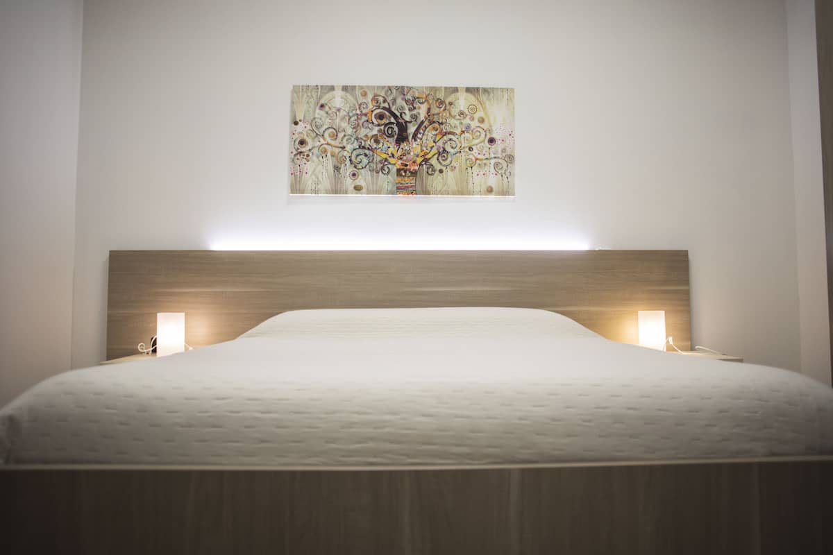 Un lit bien fait, avec une tête de lit en bois et deux lampes de chevet.