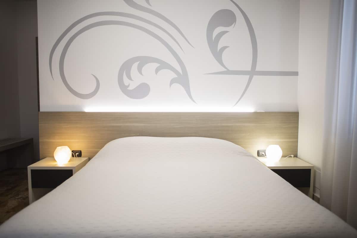 Une chambre d’hôtel avec un grand lit, deux tables de chevet avec des lampes et un mur décoratif orné de motifs abstraits.