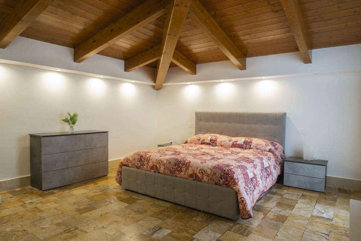 Une chambre à coucher comprenant un lit, des tables de chevet, une commode et un plafond avec des poutres en bois.