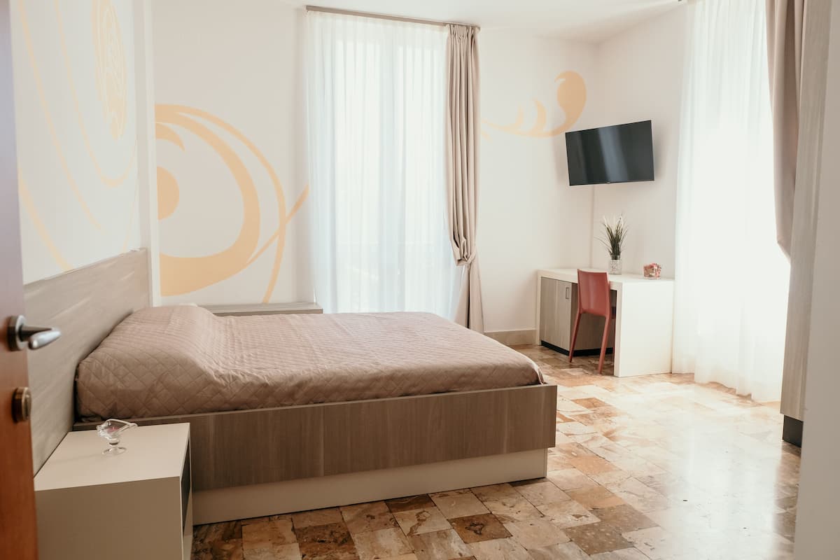 Une chambre à coucher avec un lit, une table de chevet, un bureau, une chaise et un téléviseur fixé au mur.