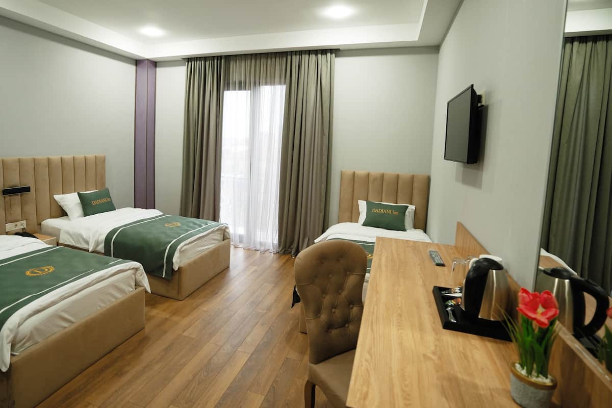 A hotel room with two beds, a wooden desk, a chair, a TV, and a window with curtains.