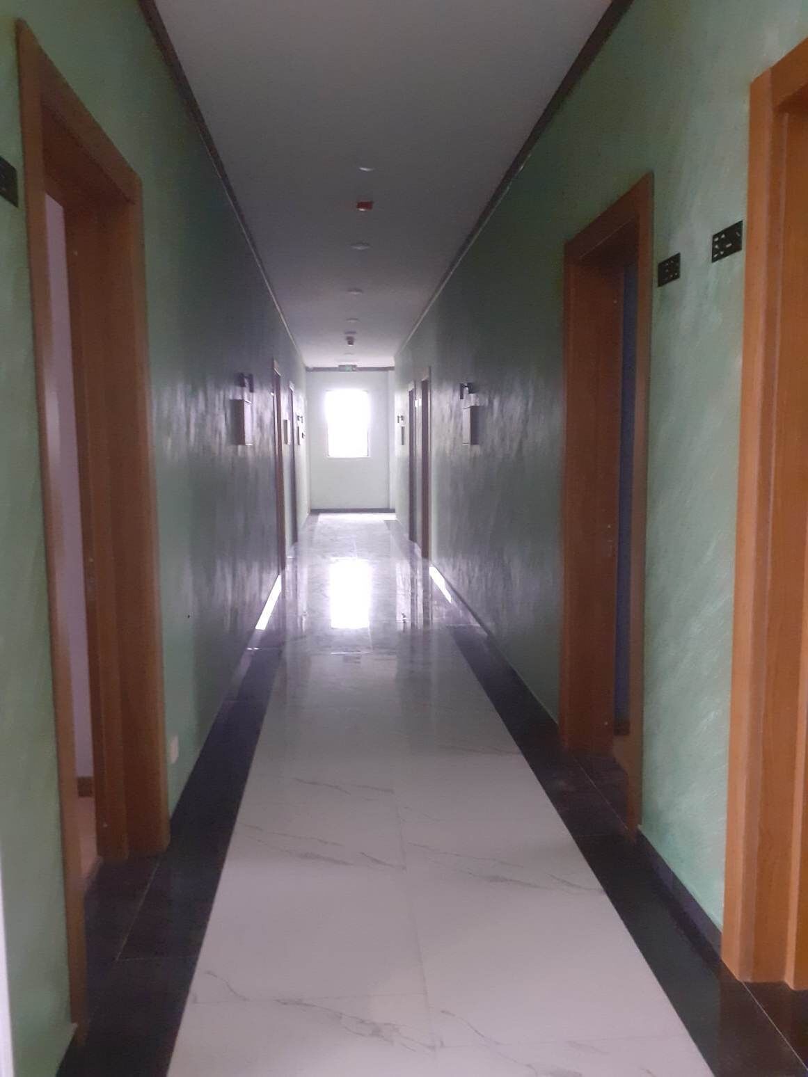 Un pasillo largo y estrecho con puertas a ambos lados, que conduce a una habitación luminosa al final.